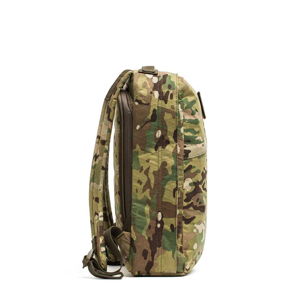 Side view of the GORUCK GR0 - X-PAC, a lightweight backpack with a camouflage pattern, made from X-PAC fabric, featuring shoulder straps and a top handle against a white background.