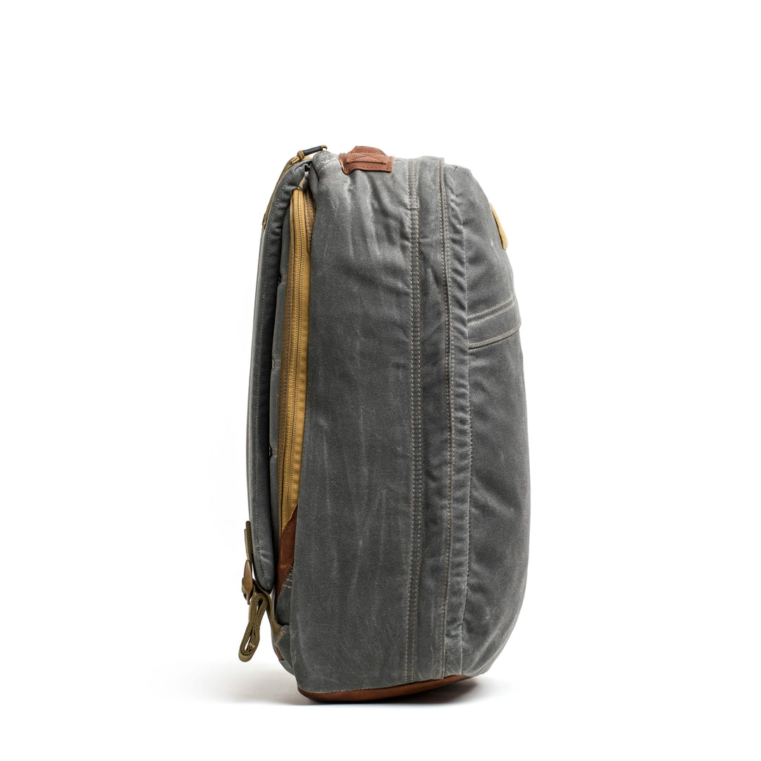 Side view of the GORUCK GR1 USA - Heritage, a gray canvas rucksack with leather accents and zippers.