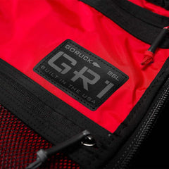 Black and red fabric backpack showcasing AquaGuard zippers and a close-up of the label "GORUCK GR1 USA - X-PAC 26L Built in the USA.