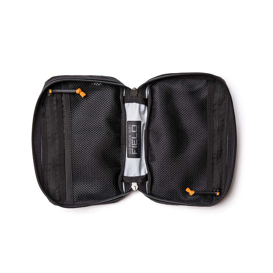 The GORUCK GR1 Field Pocket - X-PAC is a black electronics organizer with mesh pockets and bright orange AquaGuard zippers, made from waterproof fabric and shown lying flat on a white background.