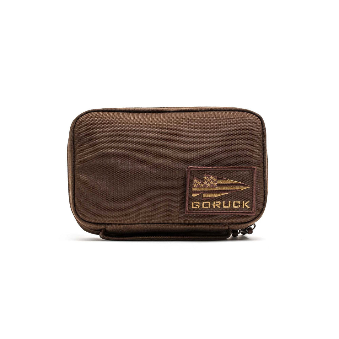 The GR1 Field Pocket is a brown rectangular pouch with a GORUCK patch and zipper, ideal as a dopp kit or for organizing camera gear, shown on a white background.