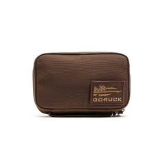 The GR1 Field Pocket is a brown rectangular pouch with a GORUCK patch and zipper, ideal as a dopp kit or for organizing camera gear, shown on a white background.