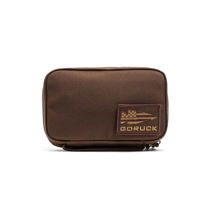 The GR1 Field Pocket is a brown rectangular pouch with a GORUCK patch and zipper, ideal as a dopp kit or for organizing camera gear, shown on a white background.