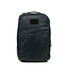 The GORUCK GR1 USA - Heritage backpack, made from Waxed Duck Canvas in black, features a front zipper and top handle, showcased elegantly against a white background.