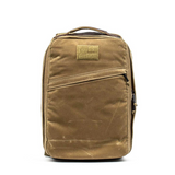 The GORUCK GR1 USA - Heritage is a stylish and functional brown backpack made from durable waxed duck canvas, featuring a minimalist design with a diagonal front zipper pocket and top handle, perfect for everyday adventures.