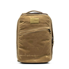 The GORUCK GR1 USA - Heritage is a stylish and functional brown backpack made from durable waxed duck canvas, featuring a minimalist design with a diagonal front zipper pocket and top handle, perfect for everyday adventures.