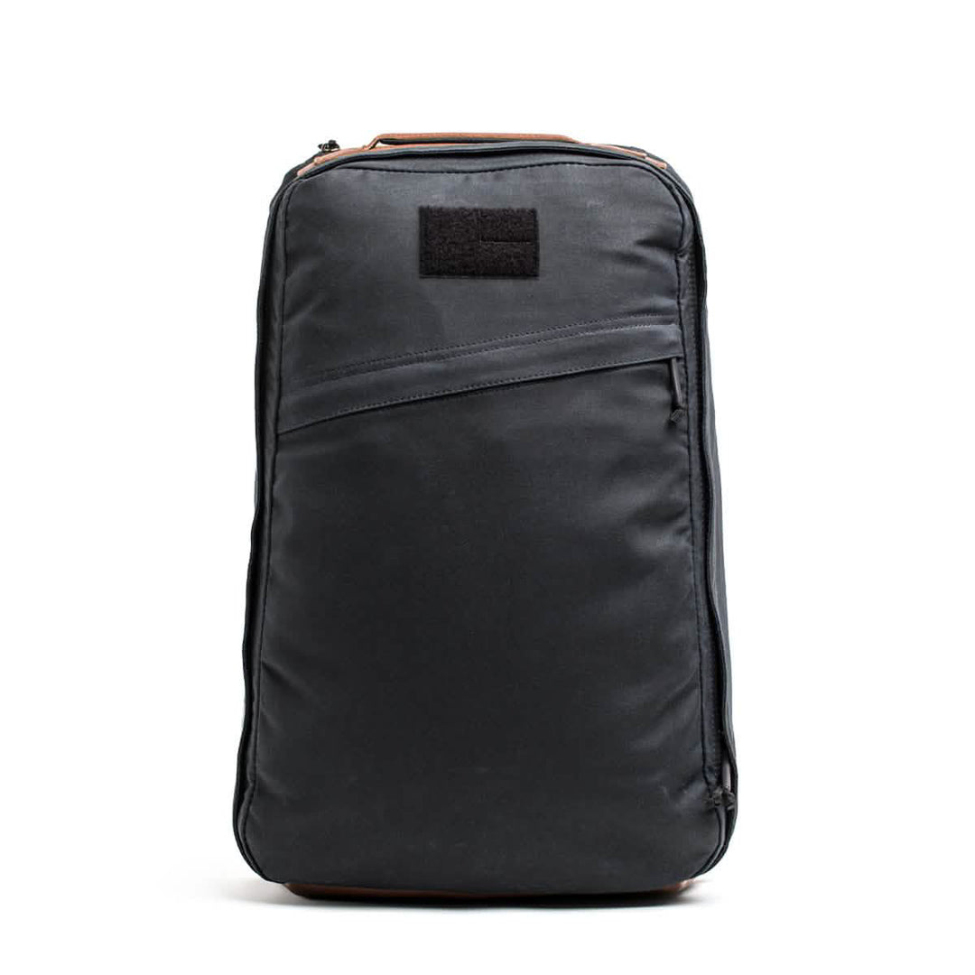 A black, rectangular GR1 USA - Heritage backpack from GORUCK, made of waxed canvas, features a top handle and front pocket on a white backdrop.