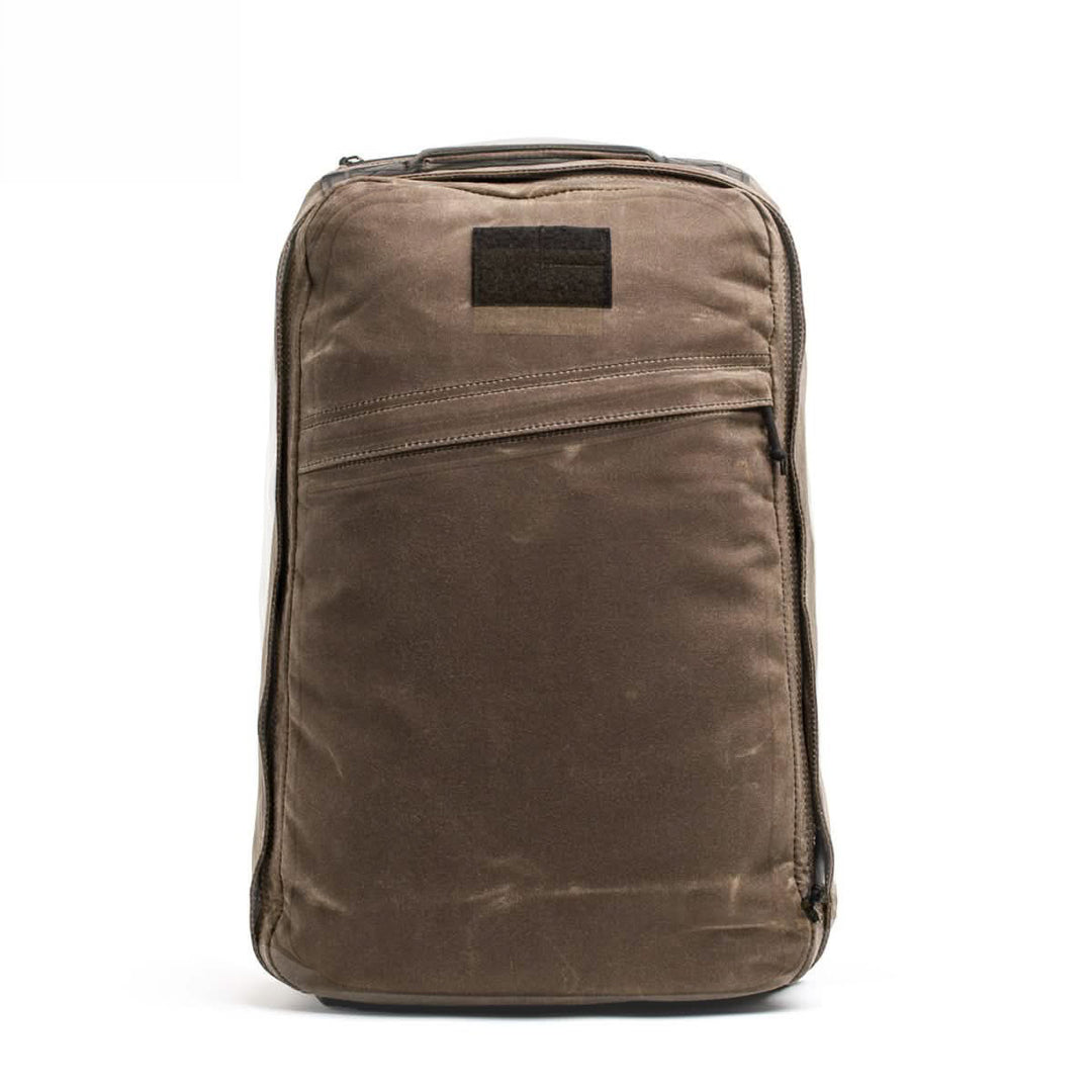 The GR1 USA - Heritage by GORUCK is a brown rectangular backpack made from durable Waxed Duck Canvas, featuring a front zipper pocket and a top handle.