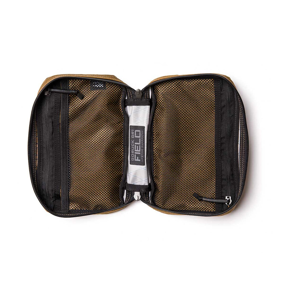 An open brown GORUCK GR1 Field Pocket - X-PAC electronics organizer with AquaGuard zippers, mesh pockets, and a small cylindrical item labeled "FIELD" inside.