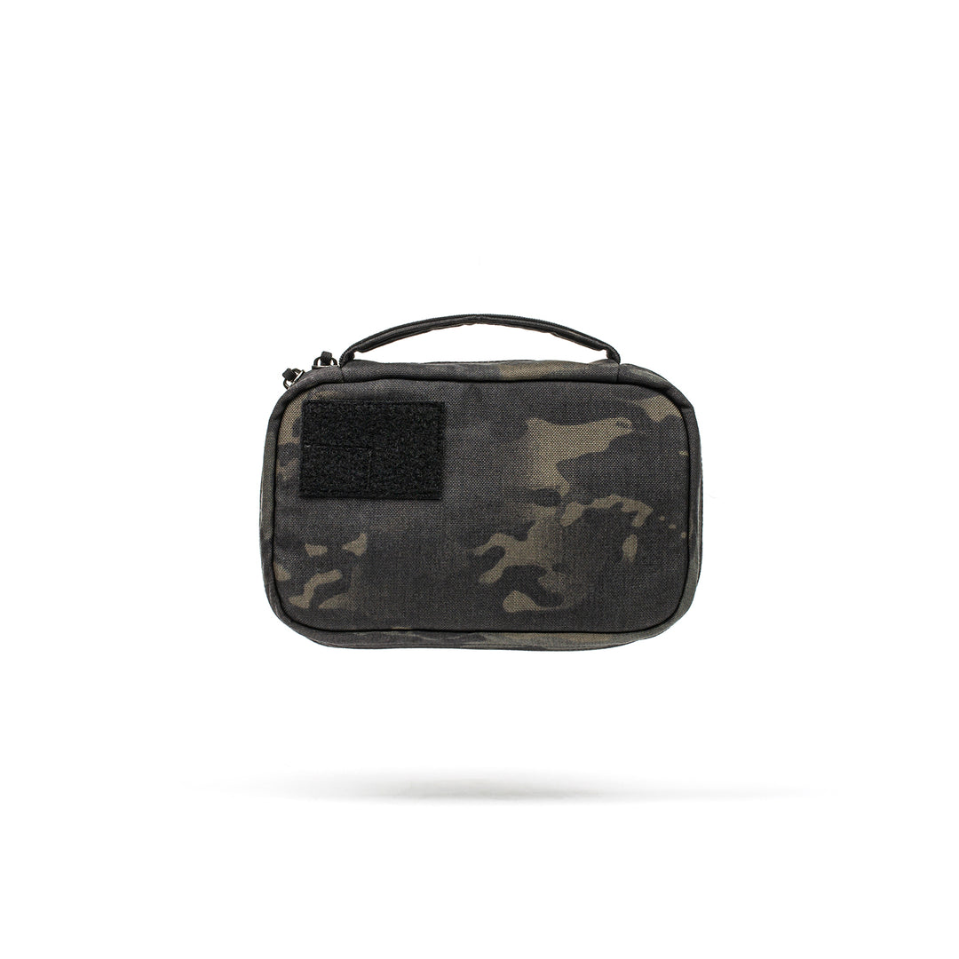 The GORUCK GR1 Field Pocket is a small, rectangular pouch with a camouflage pattern, handle, and black front patch—ideal for use as a dopp kit or electronics organizer.
