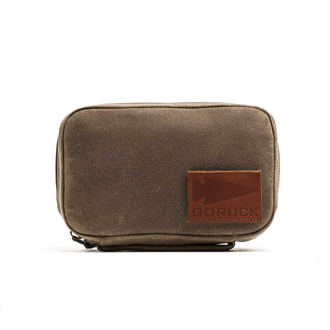 The GORUCK GR1 Field Pocket - Waxed Canvas is a small, rectangular brown pouch made from waxed duck canvas with a leather GORUCK patch—ideal for use as a rugged rucksack organizer.