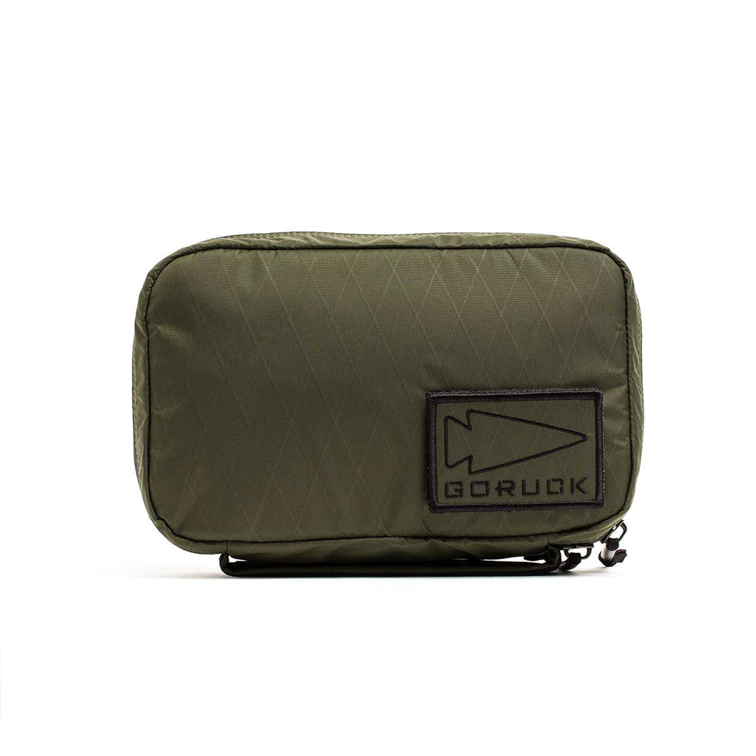 The GORUCK GR1 Field Pocket - X-PAC is an olive green, waterproof zippered pouch with a black patch featuring the arrowhead logo—perfect for organizing electronics.