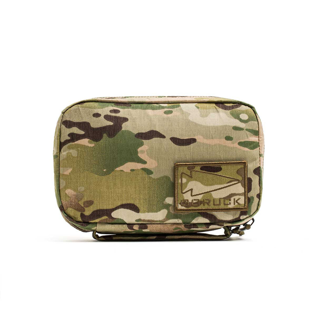 The GORUCK GR1 Field Pocket - X-PAC is a small, waterproof camouflage pouch with a Velcro patch showing a white mountain and “GORUCK.” Perfect for organizing electronics and everyday essentials.