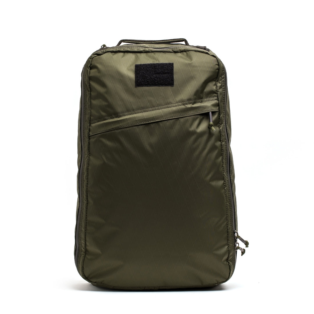 The GORUCK GR1 USA - X-PAC backpack features an olive green color with a diagonal AquaGuard zipper pocket and top handle, crafted from durable X-PAC material, set against a plain white background.