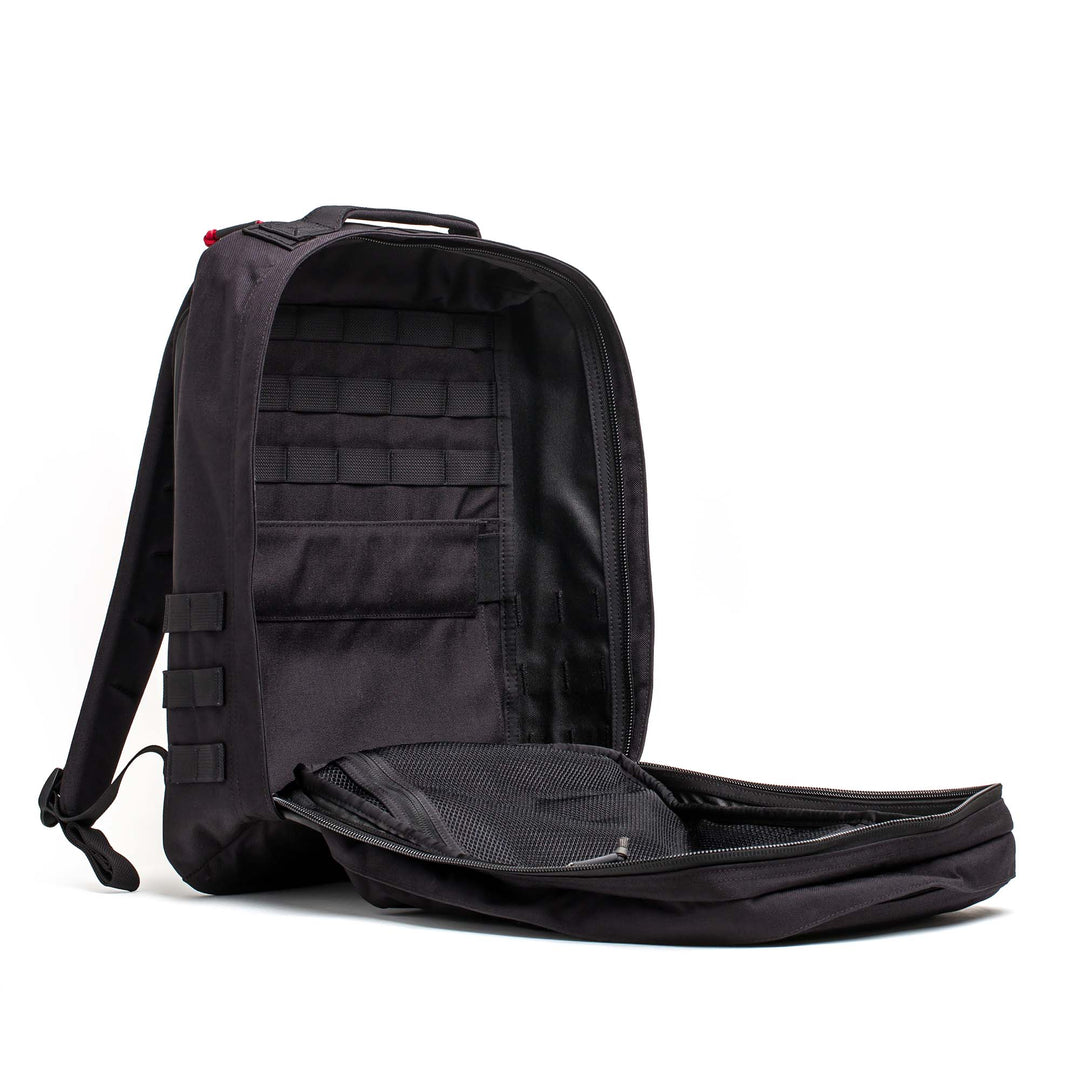 A black GORUCK GR2 rucksack is shown open, revealing its roomy interior and multiple compartments—ideal for use as a carry-on travel bag.