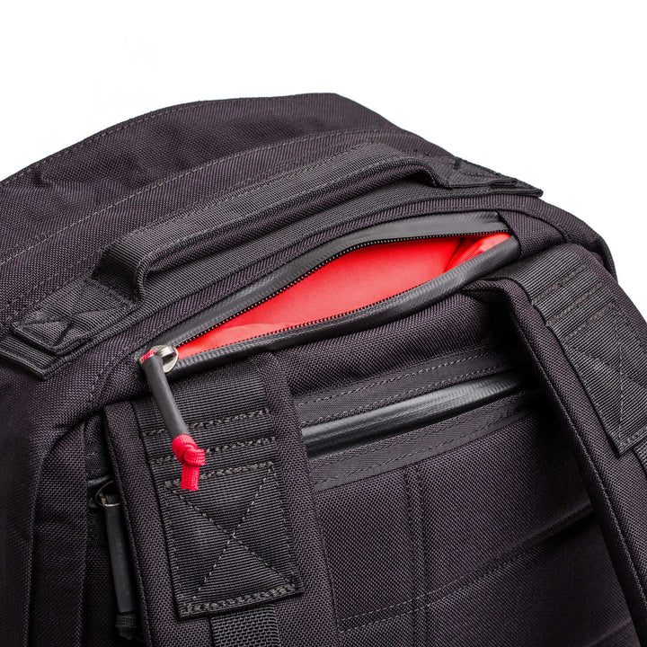 The GORUCK GR2 is a black rucksack featuring a partially open zipper that reveals a bright red interior pocket—designed as the ideal carry-on travel bag.