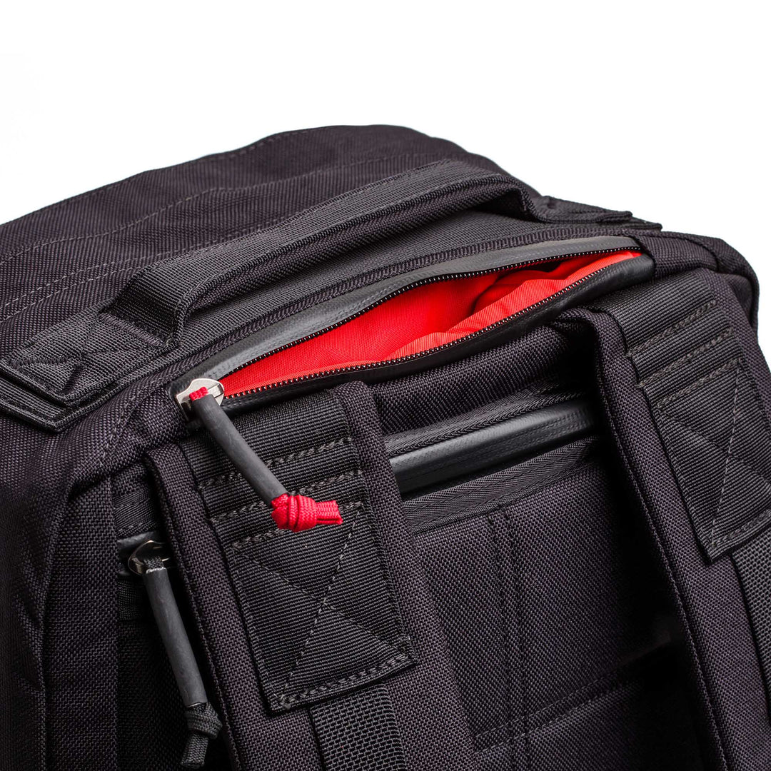 Close-up of the GORUCK GR2 black carry-on backpack, featuring a red interior, padded shoulder straps, and partially open zipper—design inspired by the original GR2 ruck.