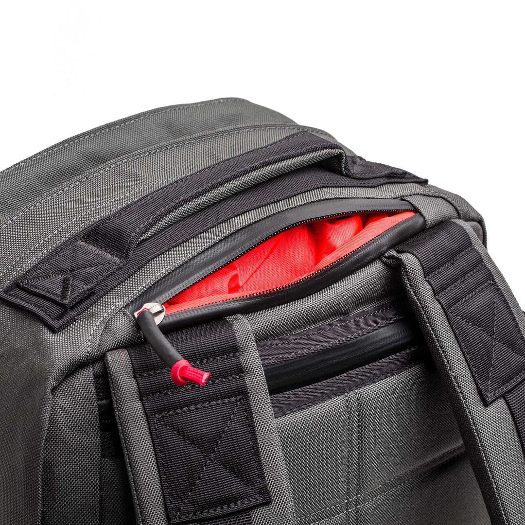 Close-up of the GORUCK GR2 black backpack with a partially open zipper, showing its bright red inner lining.