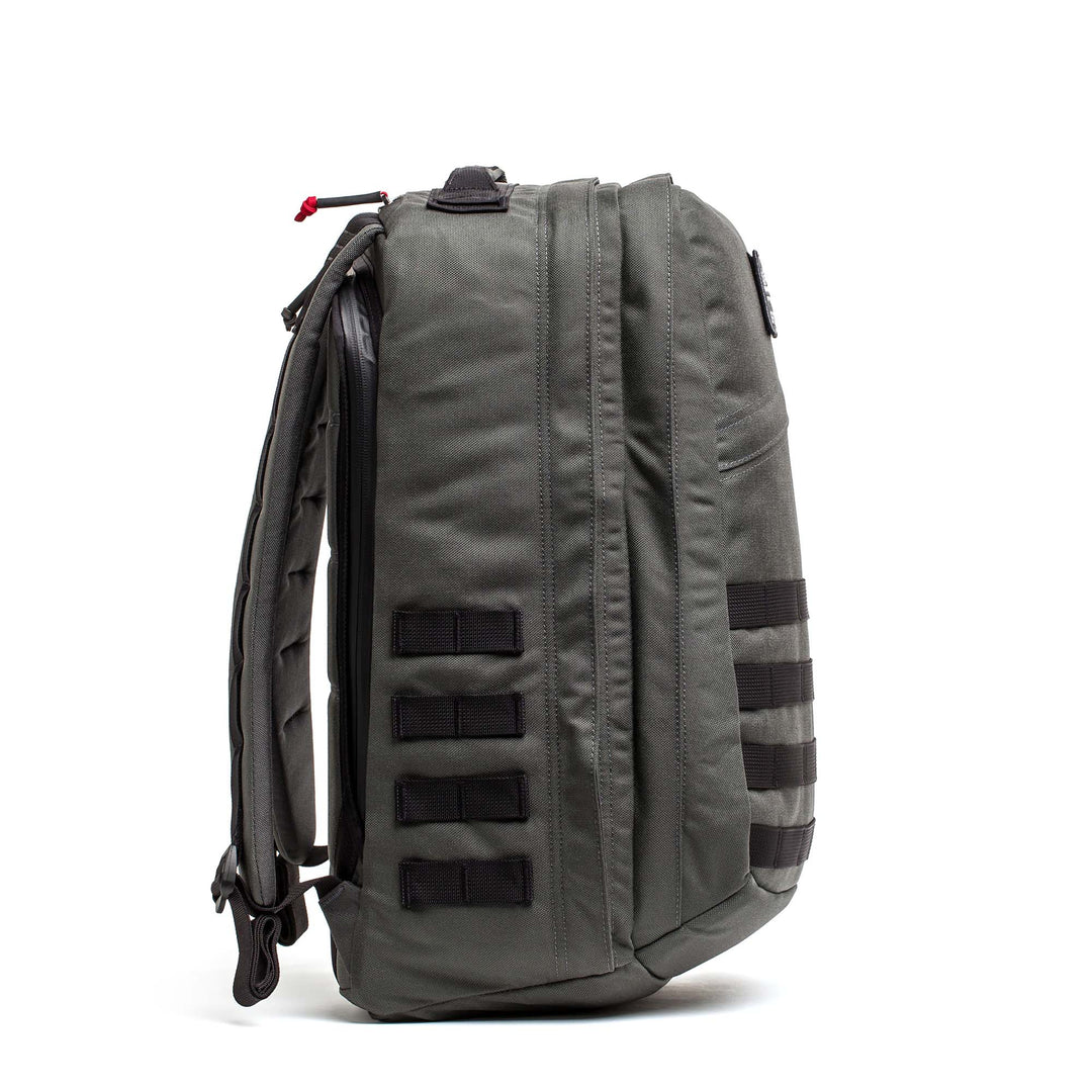 Side view of the GORUCK GR2 gray carry-on backpack with black webbing loops and padded shoulder straps, standing upright.