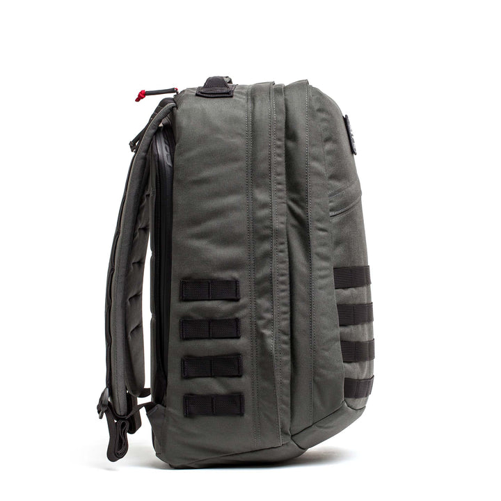 Side view of the GORUCK GR2 gray carry-on backpack with black webbing loops and padded shoulder straps, standing upright.
