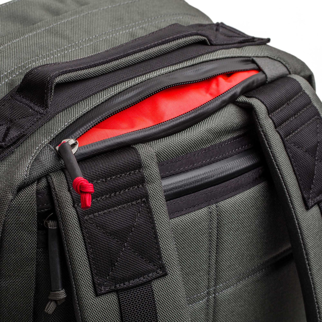 Close-up of the GORUCK GR2 dark gray carry-on backpack with a partially open pocket revealing its bright red interior lining.