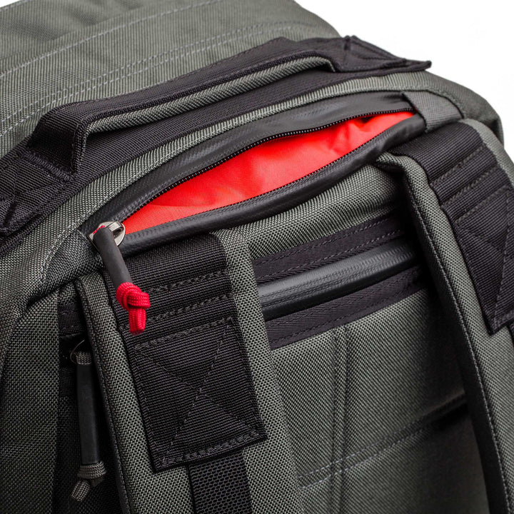 Close-up of the GORUCK GR2 dark gray carry-on backpack with a partially open pocket revealing its bright red interior lining.