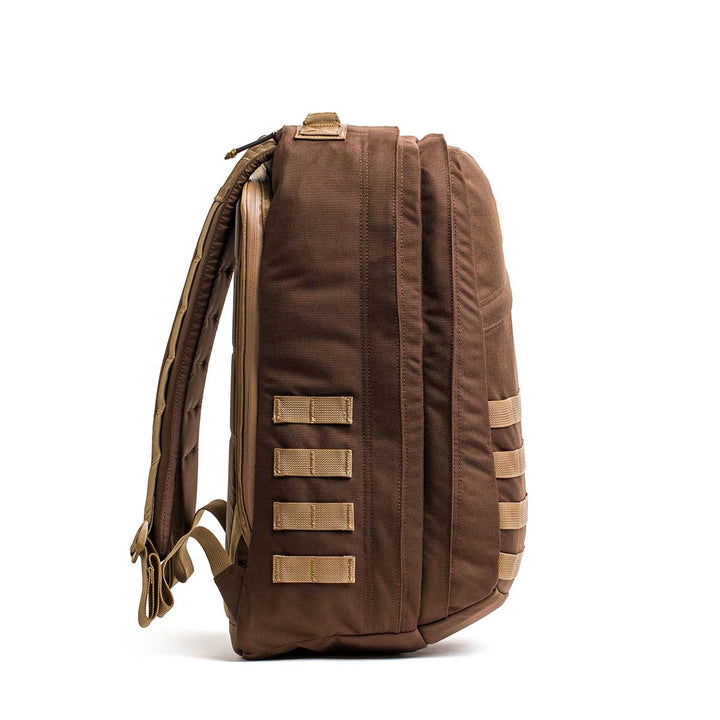 The GORUCK GR2 is a brown travel backpack with tan straps and multiple loops, shown from the side against a white background; designed to be carry-on compliant for convenience.