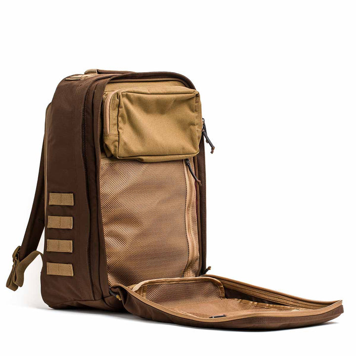 The GORUCK GR2 travel backpack, shown in brown and tan with an open front panel revealing a mesh pocket and inner compartments, is carry-on compliant for convenient journeys.