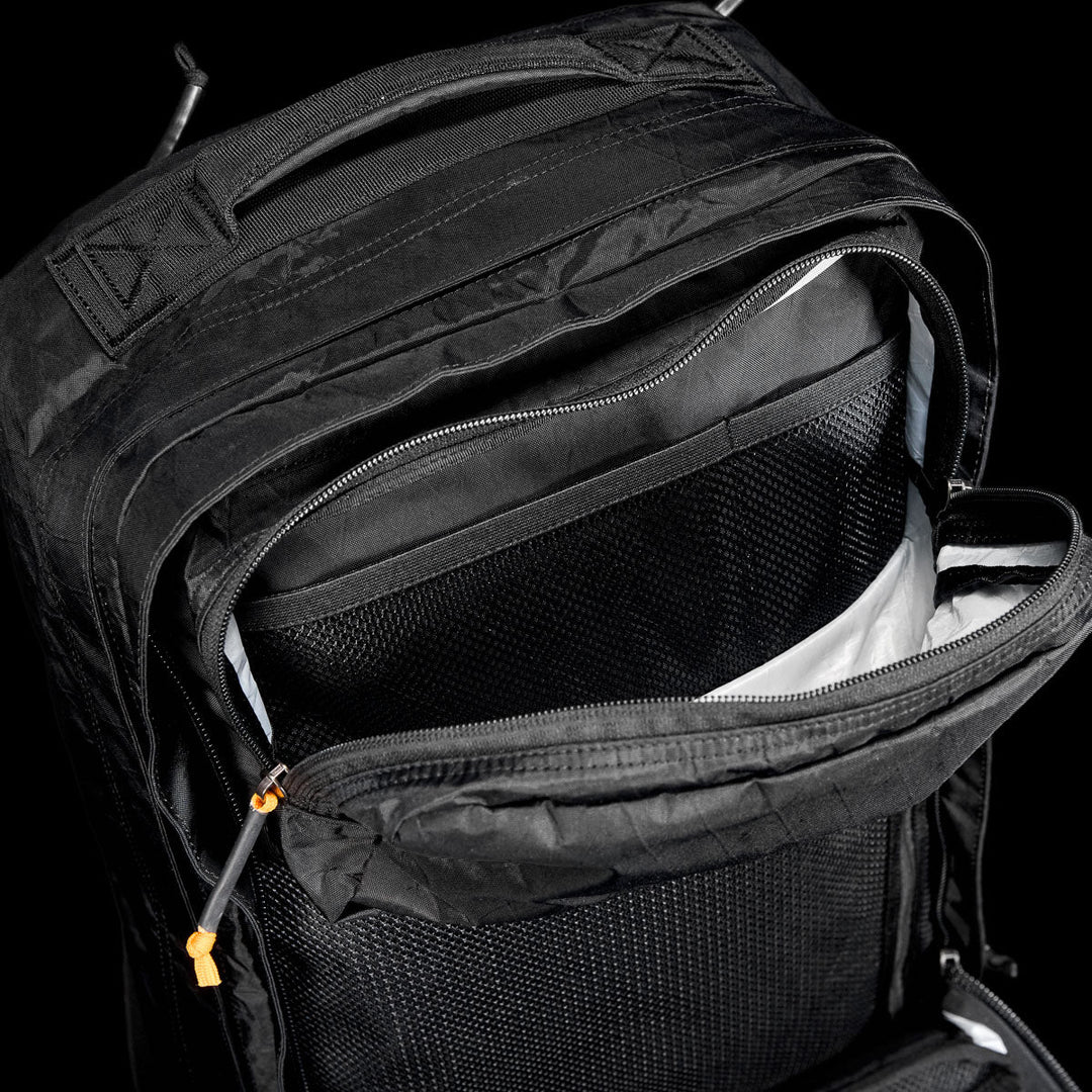 Open black GR2 X-PAC backpack by GORUCK reveals interior pockets and compartments with orange zipper pulls—a rugged, weatherproof pack designed to keep your essentials safe and organized.