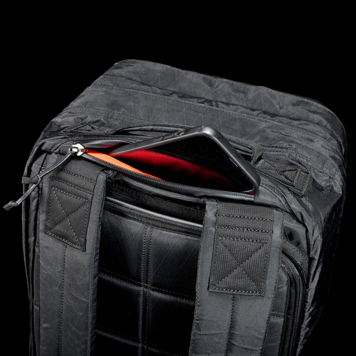 GORUCK black rucksack with visible padded straps and zippered pocket open to reveal a phone