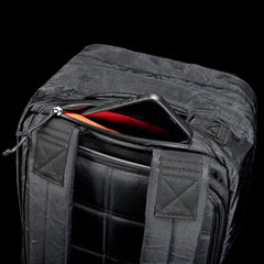 GORUCK black rucksack with visible padded straps and zippered pocket open to reveal a phone