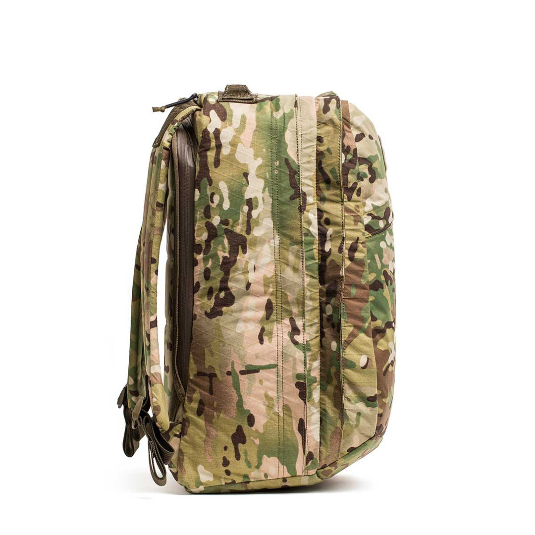 A side view of the GORUCK GR2 X-PAC, a waterproof backpack with a camouflage pattern, zippers, and shoulder straps, shown standing upright.