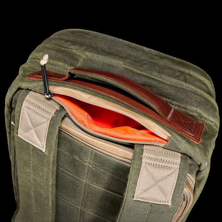 The GORUCK GR2 - Heritage Waxed Canvas is a green backpack with tan straps, a Red Wing leather handle, and an orange-lined top zipper pocket—ideal as your go-to travel ruck.