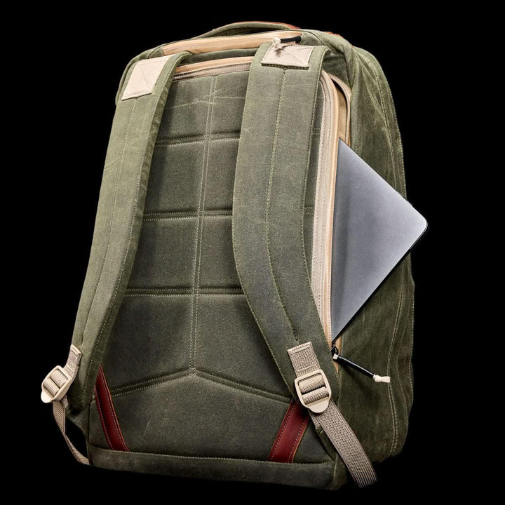 The GORUCK GR2 - Heritage Waxed Canvas backpack, shown in green with tan straps and Red Wing leather accents, features a partially visible laptop in the back zipper pocket against a black background.