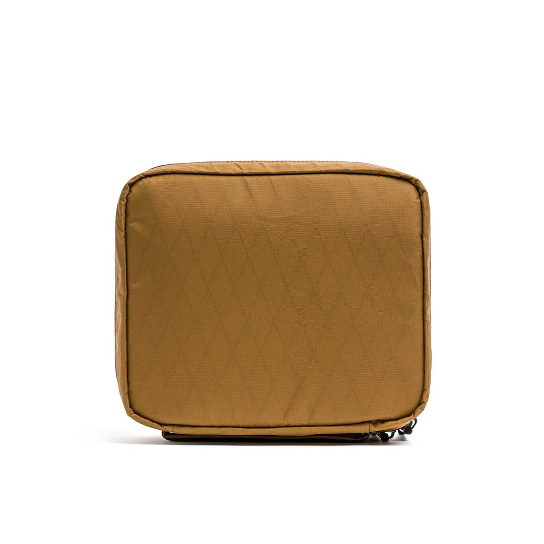 The GORUCK GR2 Field Pocket - X-PAC is a tan, square zippered pouch made from waterproof fabric with a subtle diamond pattern, perfect for protecting camera gear or organizing electronics. Pictured on a white background.