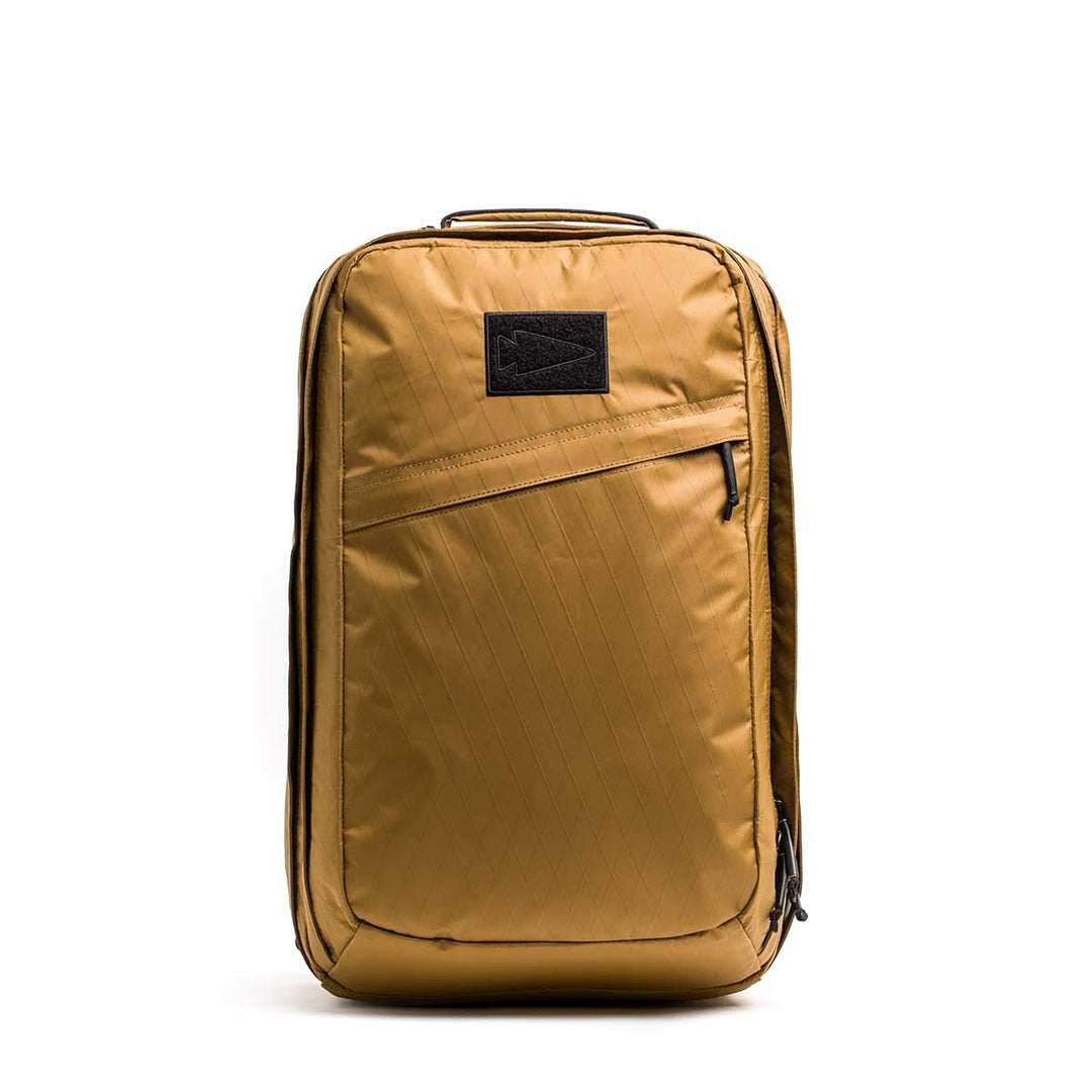 The GORUCK GR2 X-PAC is a golden brown, waterproof backpack featuring a front diagonal zipper pocket and black patch, shown upright on a white background—built for any adventure.