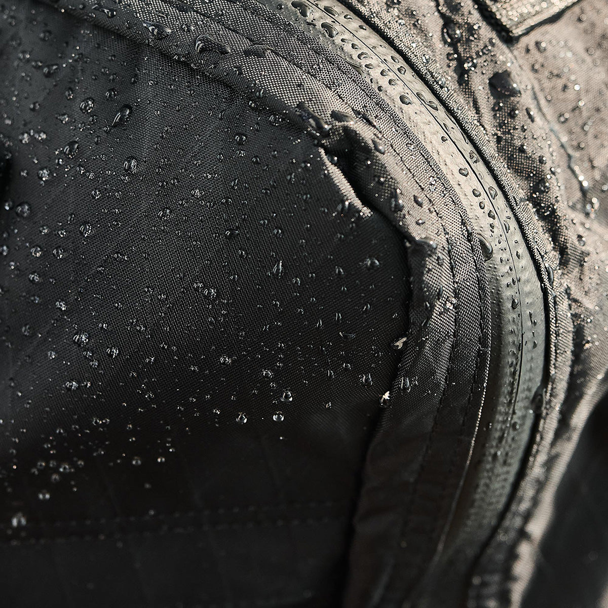 Close-up of water droplets on a black, water-resistant fabric with a sealed zipper.