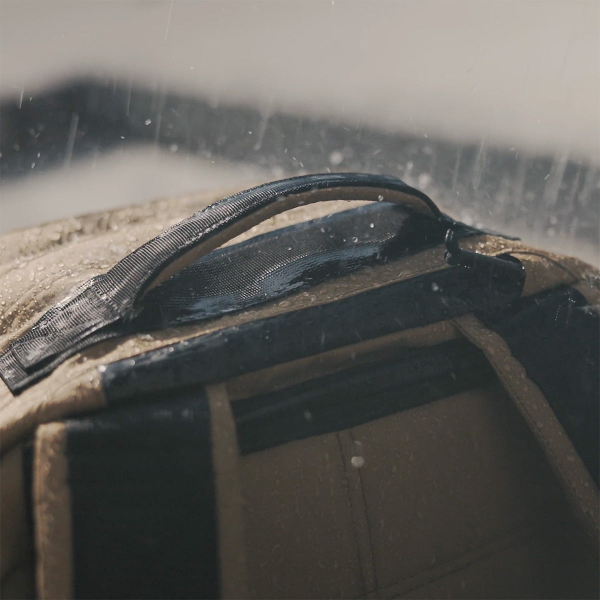 Close-up of a wet backpack handle with raindrops falling on it.