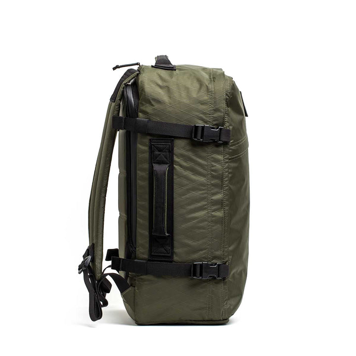 The GR3 - X-PAC olive green carry-on backpack stands upright in a side view, showing black straps and a handle; it includes a convenient laptop compartment.