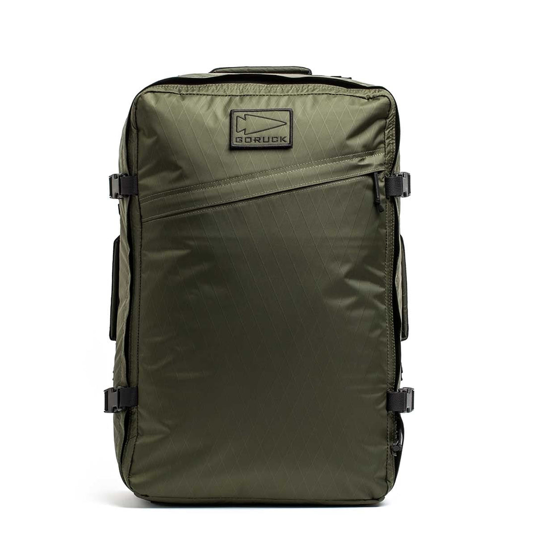 The GR3 - X-PAC is an olive green carry-on backpack featuring side buckles, a diagonal front zipper, waterproof material, and a GORUCK logo patch on top.