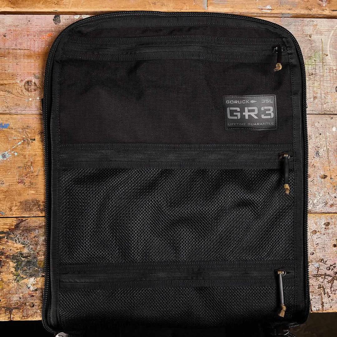 Open black GORUCK GR3 - Cordura carry-on rucksack with mesh and waterproof zippered pockets, displayed on a worn wooden surface.