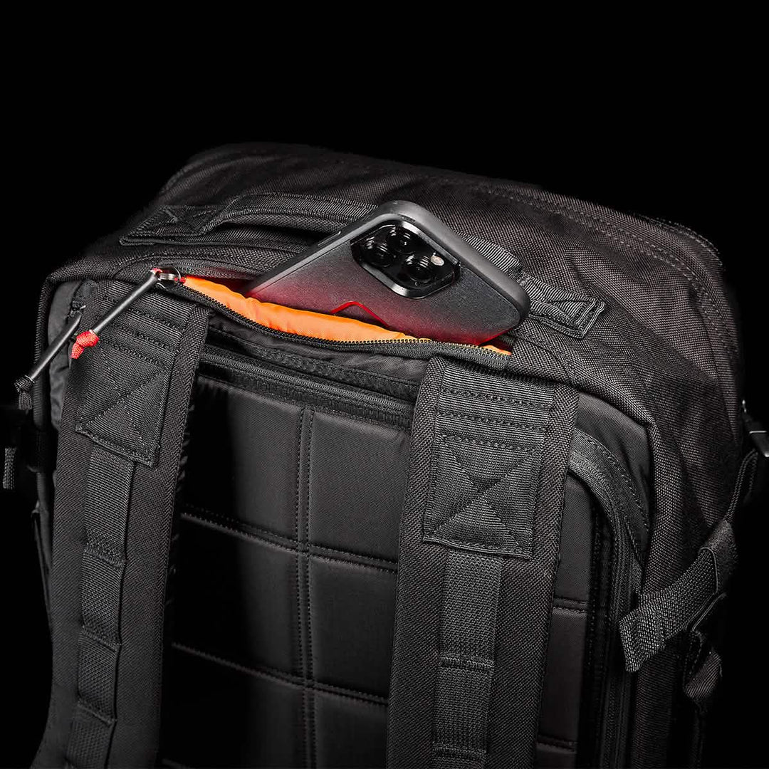 The GORUCK GR3 - Cordura is a black travel backpack featuring waterproof zippers and an orange-lined top pocket with a phone partially visible.