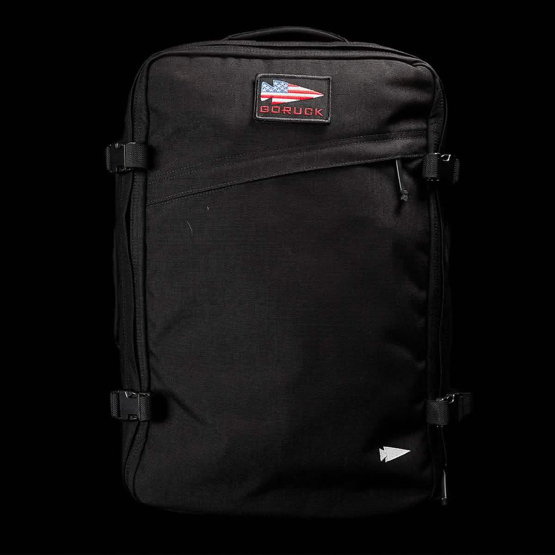 The GORUCK GR3 - Cordura is a black backpack with an American flag patch and "GORUCK" text, featuring waterproof zippers. Durable and reliable, it's ideal as a travel backpack or carry-on rucksack. Shown against a black background.