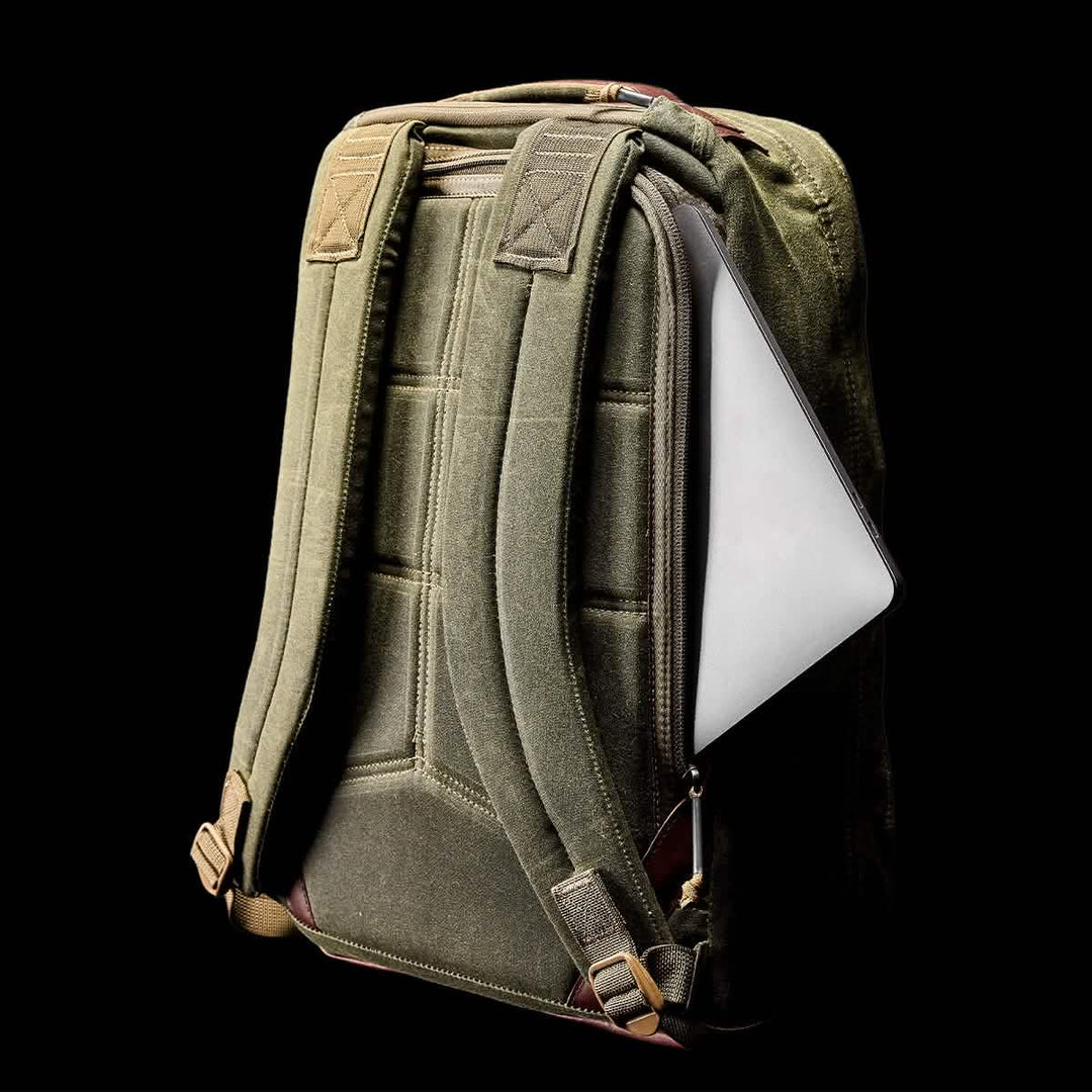 The GR1 USA - Heritage by GORUCK, a retro canvas rucksack in rich green, showcases a partially visible tablet emerging from its waxed duck canvas side pocket against a black background.