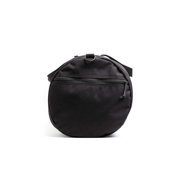 The Gym Bag - Cordura is a round black shoulder bag made from durable 1000D CORDURA, featuring a front zipper pocket and a small top strap, displayed against a white background.