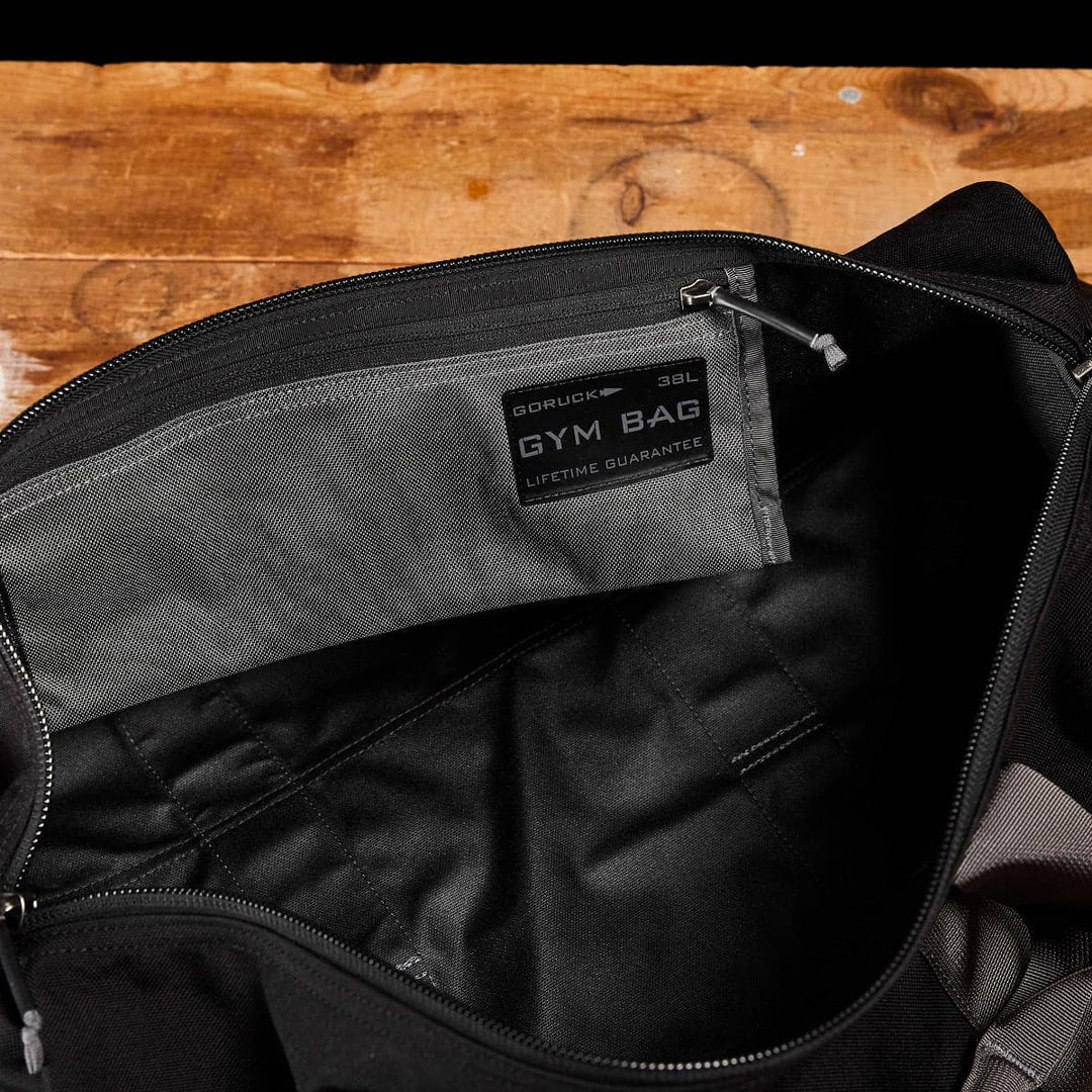 A black GORUCK Cordura gym bag, known for its durability, sits on a wooden surface with the interior label visible, showcasing the brand and 38L size details.