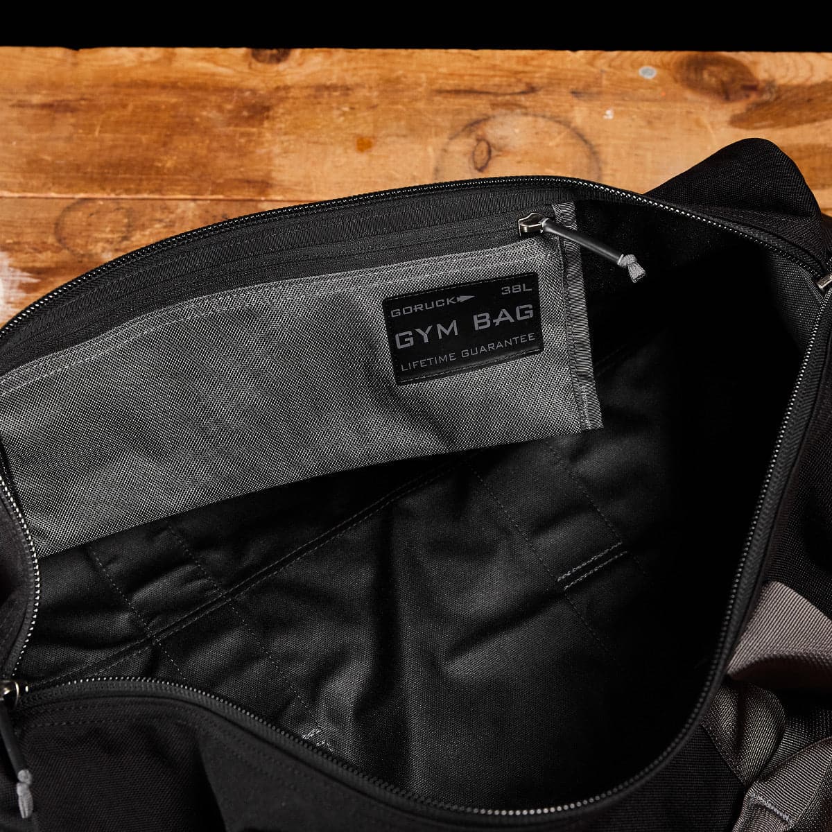 A black GORUCK Cordura gym bag, known for its durability, sits on a wooden surface with the interior label visible, showcasing the brand and 38L size details.