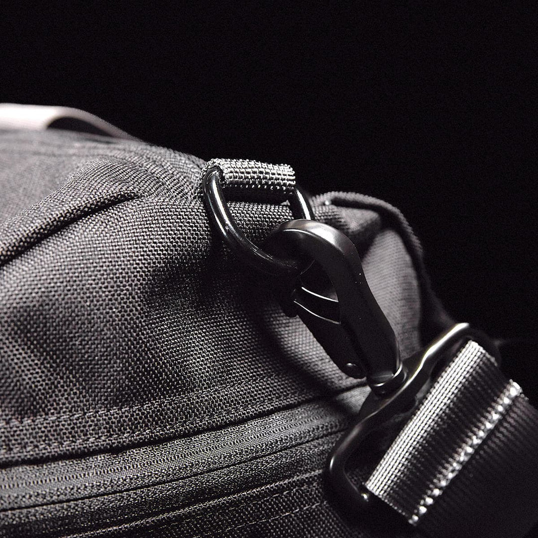 Close-up of the Gym Bag - Cordura by GORUCK, featuring a sleek black fabric design made from durable CORDURA, complete with a metal clasp and adjustable strap, set against a black background.
