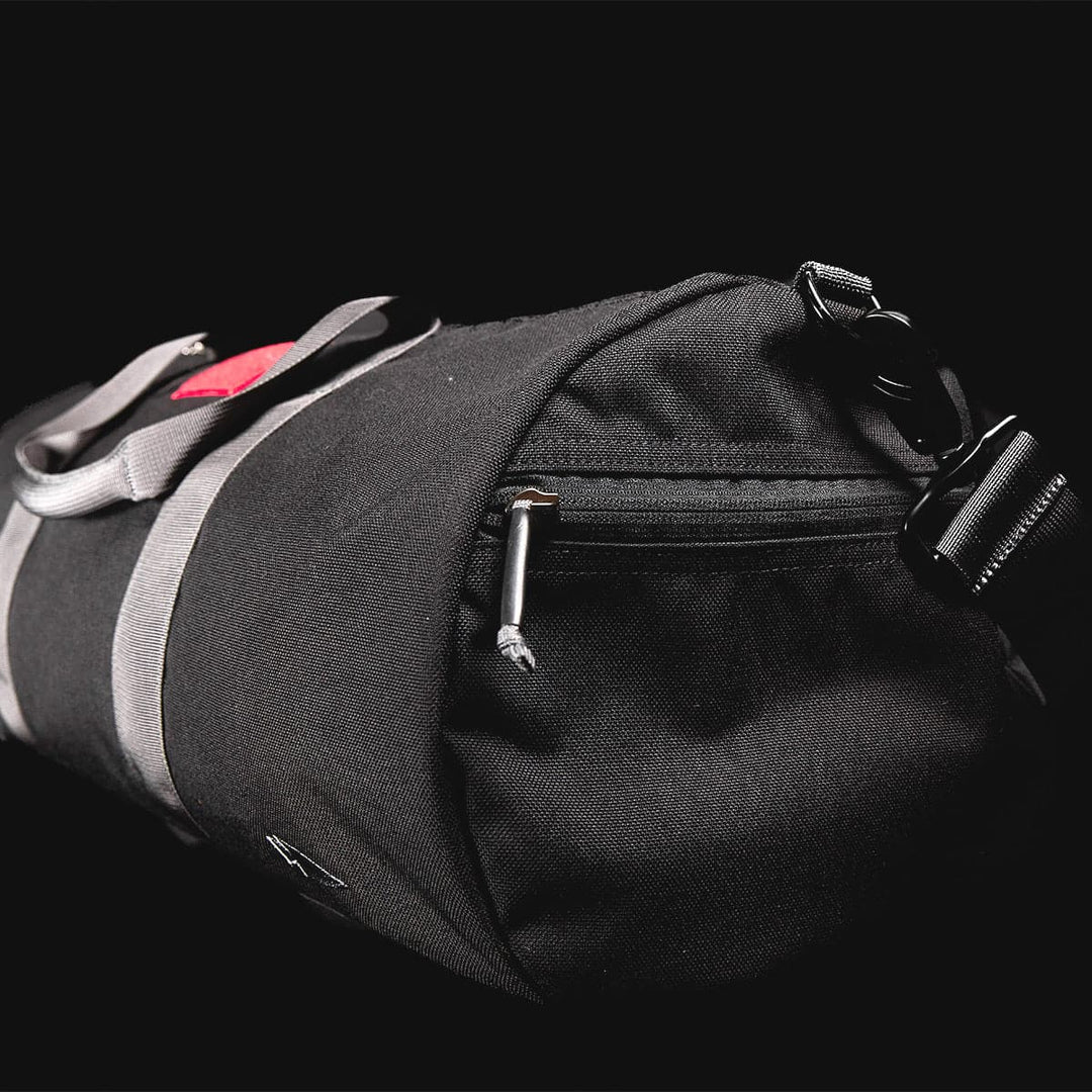 Close-up of the Gym Bag - Cordura by GORUCK, crafted from durable black CORDURA and featuring gray straps and a zipper, accented with a small red patch on a black background. The 38L capacity provides ample space for all your essentials.