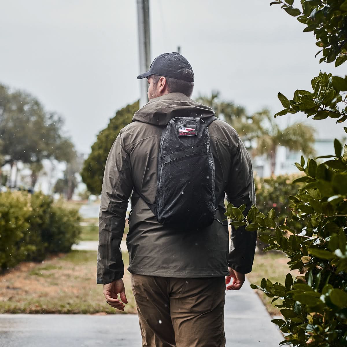 Man rucking outdoors in rain wearing GORUCK black packable backpack and jacket